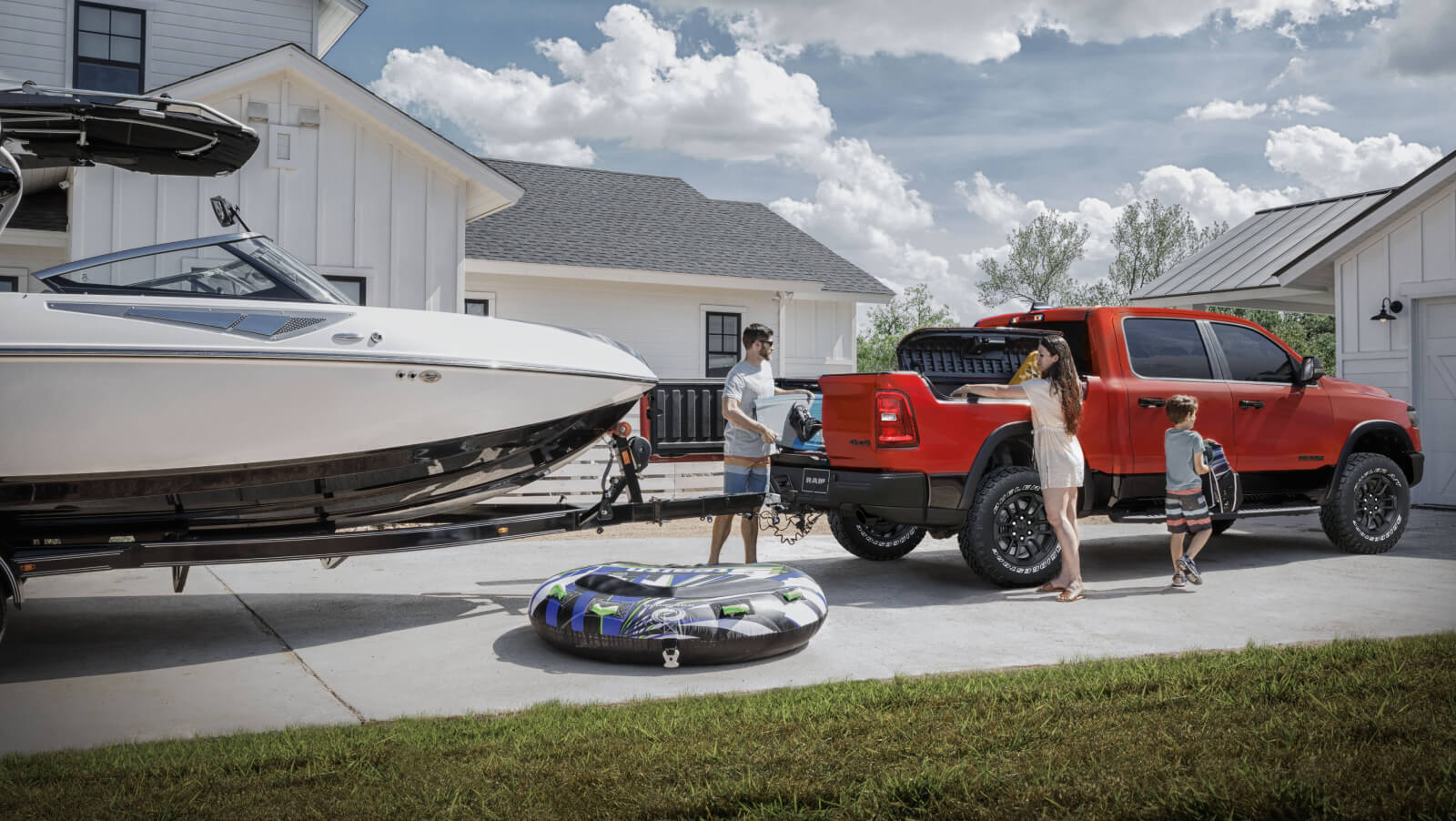 2025 Ram 1500 Rebel in Flame Red and Diamond Black Crystal, parked in driveway in front of a house and garage with a boat on a trailer and a family loading it