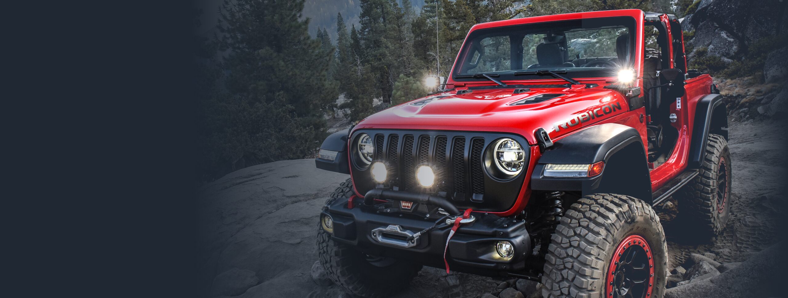 The 2022 Jeep Wrangler Rubicon being driven off-road. It has been equipped with aftermarket lighting on its grille and at the base of its windshield.