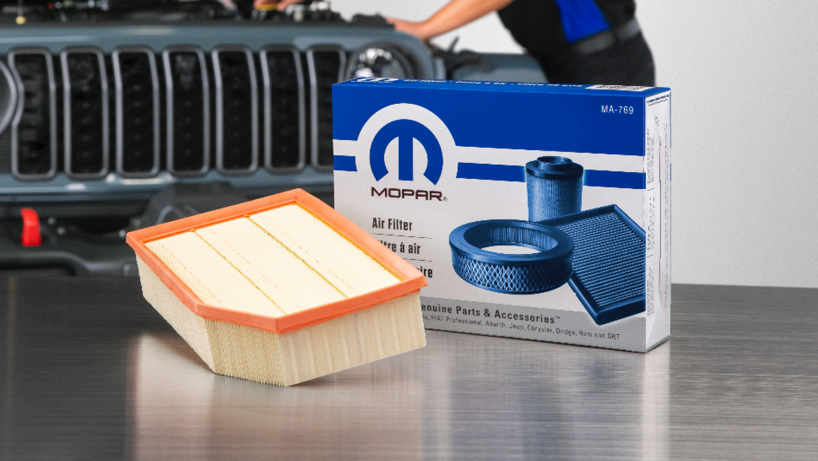 Filtro de aire Mopar sobre una mesa metálica, delante de la caja del filtro de aire Mopar con el número de referencia y un Jeep al fondo
