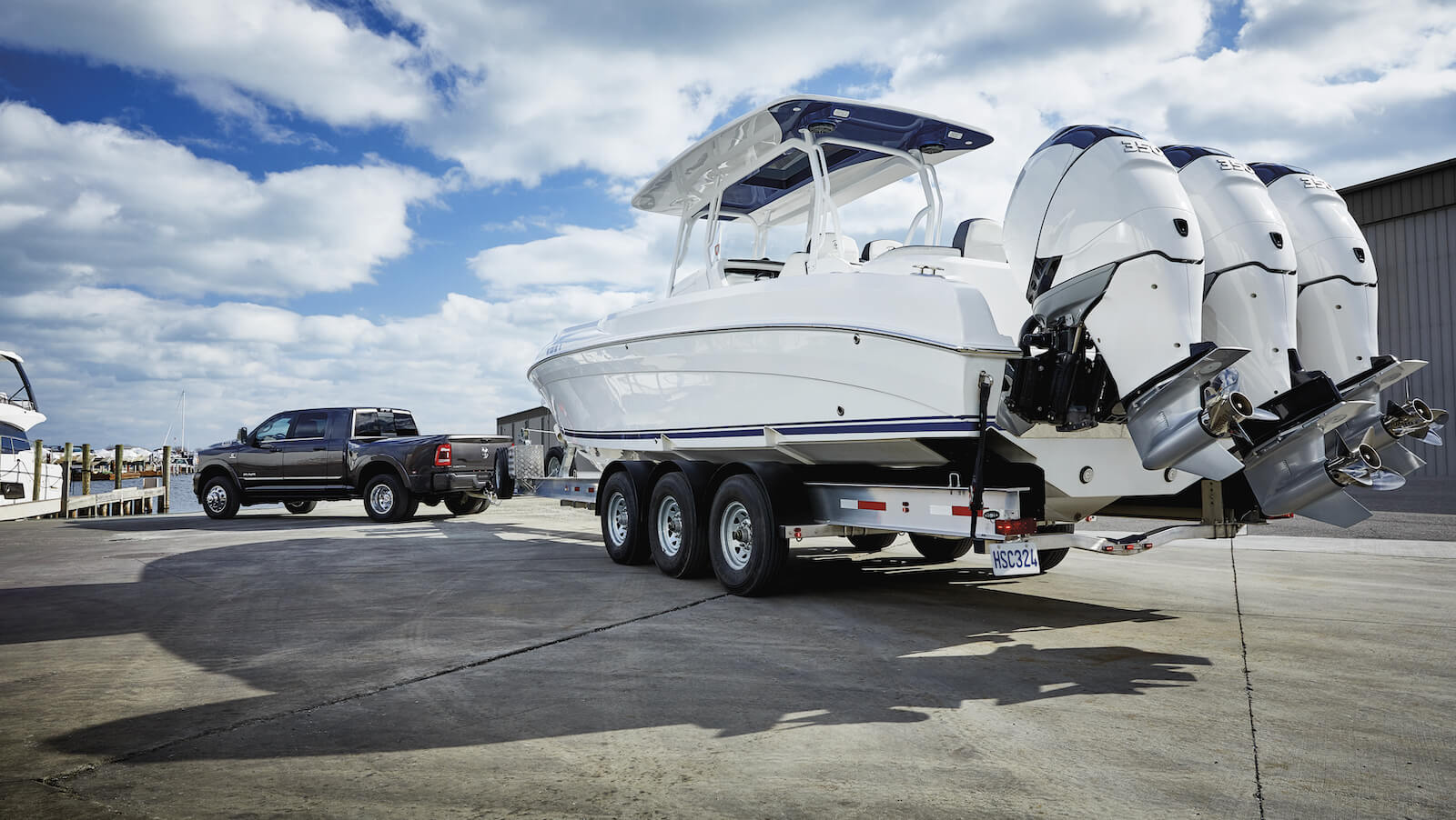 Ram 3500 Limited Dually 2023 en color Granite Crystal Pearl, con un barco de pesca grande a remolque, estacionada en un puerto deportivo