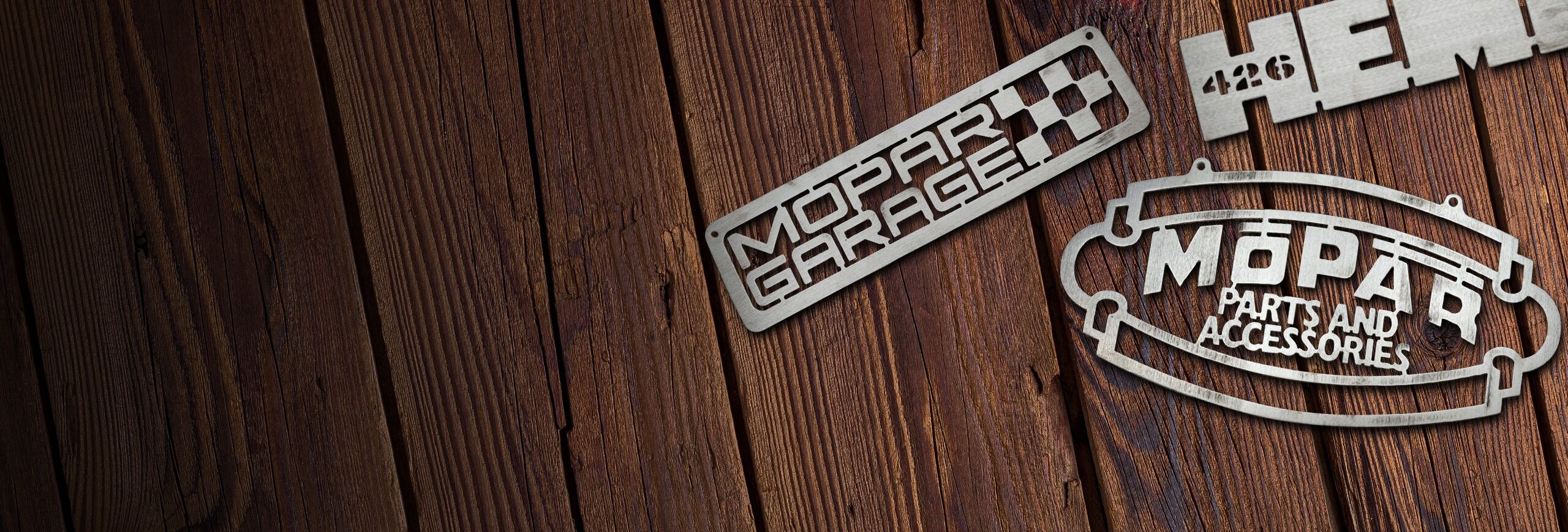Un juego de tres emblemas dispuestos en una superficie de madera: un emblema de Mopar Garage, un emblema de Mopar Parts and Accessories y un emblema de Hemi 426.